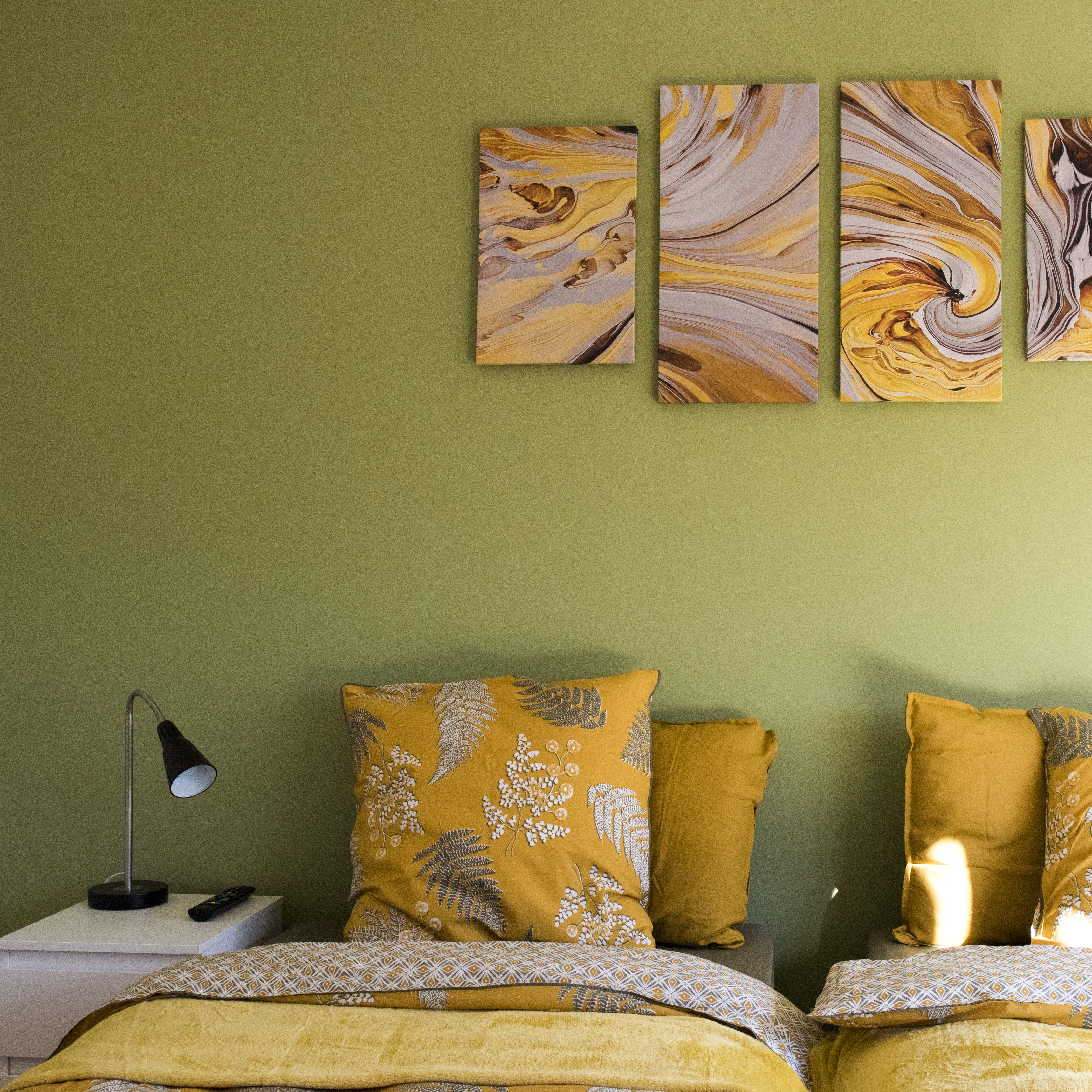 Chambre avec murs verts et literie jaune. Tableau abstrait de tâches jaunes et grises au mur.